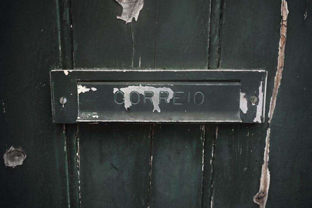 A close-up of an old mail slot labeled 'CORREIO' on a weathered green wooden door.
